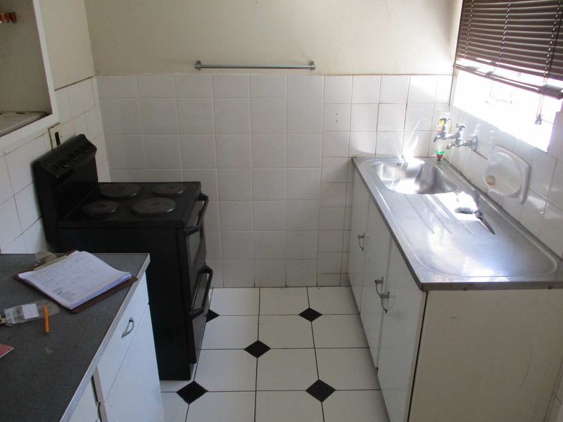 A compact, dated kitchen featuring a stainless steel sink, tiled splashback, and a freestanding stove, offering potential for a modern renovation.