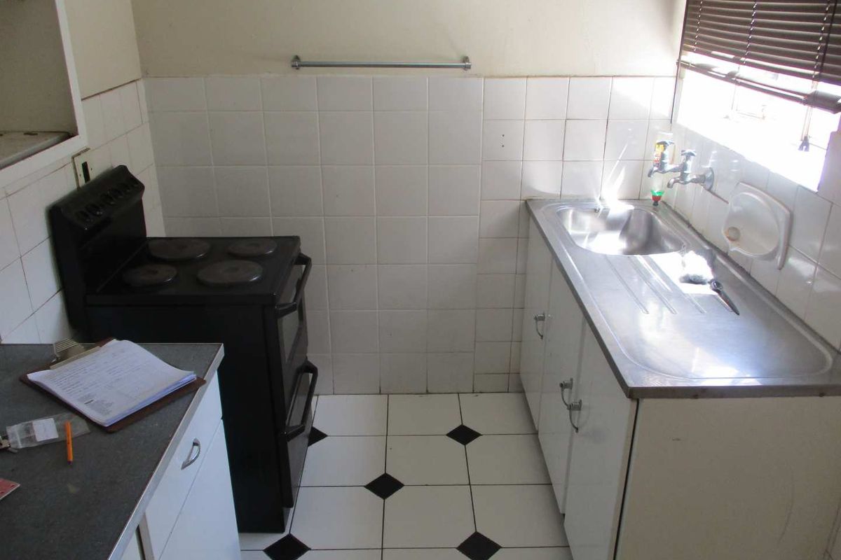 A compact, dated kitchen featuring a stainless steel sink, tiled splashback, and a freestanding stove, offering potential for a modern renovation.