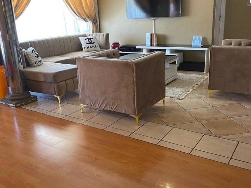 Spacious living area featuring a combination of laminate and ceramic tile flooring, a decorative column, and neutral wall tones.