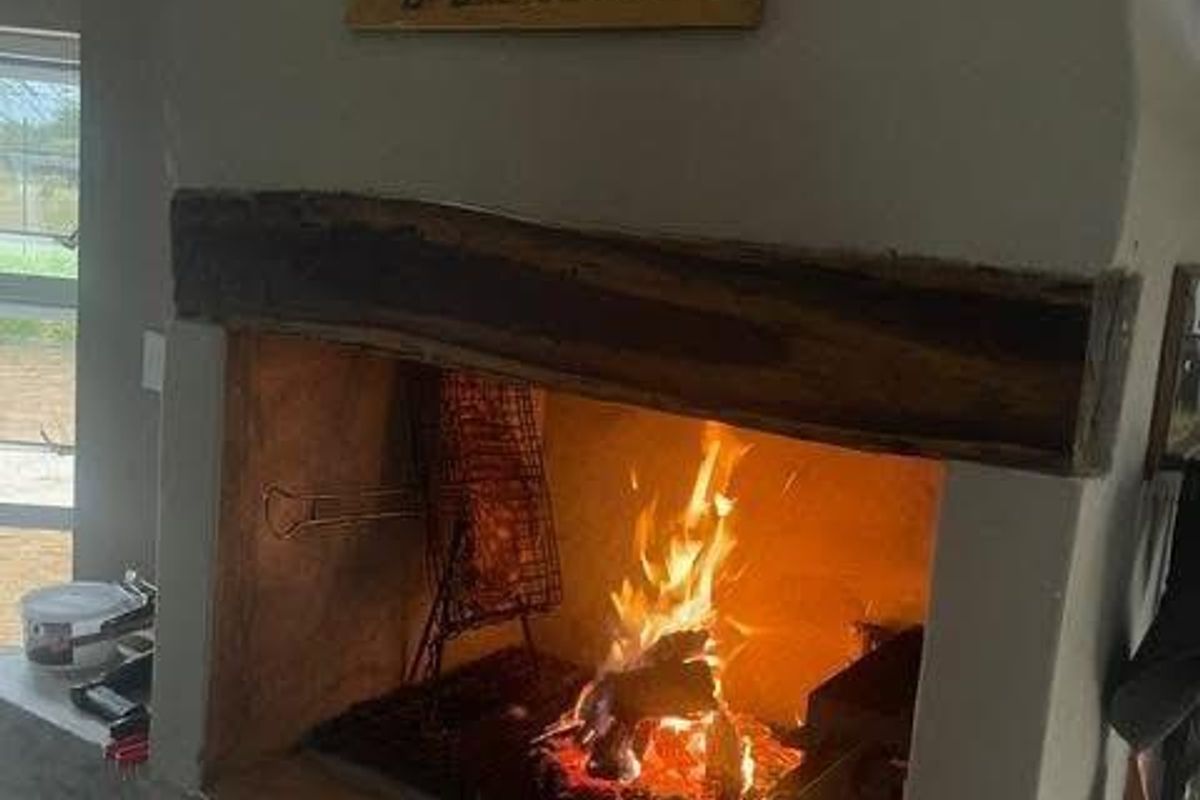 A built-in indoor fireplace featuring a rustic timber mantel and a masonry surround, currently in use with a fire burning.