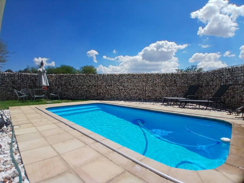 A private swimming pool area featuring a paved deck and a decorative gabion stone boundary wall.