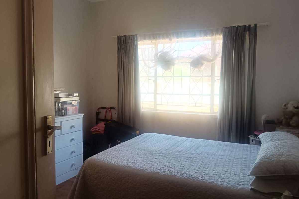 A standard bedroom featuring a window with security bars and curtain rails, providing natural light and basic functional space.