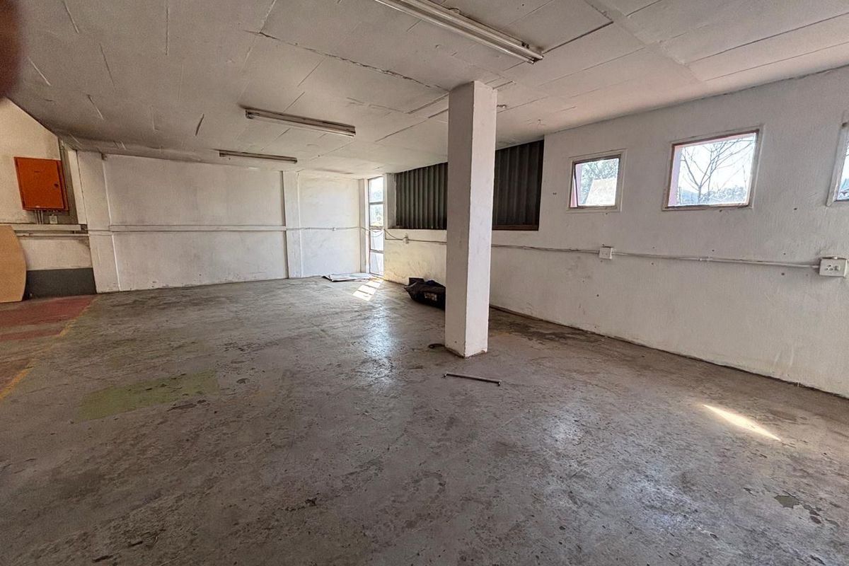 An empty industrial utility space featuring concrete flooring, exposed structural columns, and surface-mounted electrical conduits, suitable for storage or workshop use.