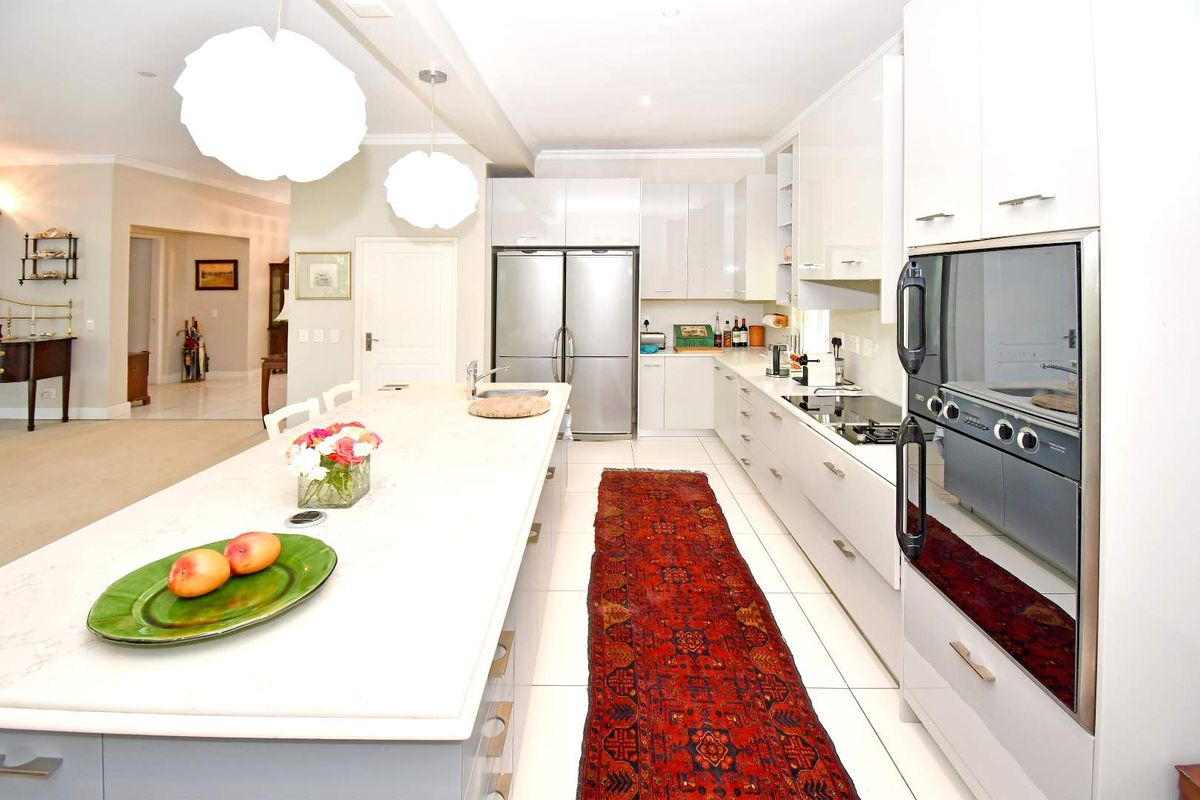 Modern kitchen featuring a large central island with stone countertops, sleek white cabinetry, integrated double ovens, and a smooth cooktop.