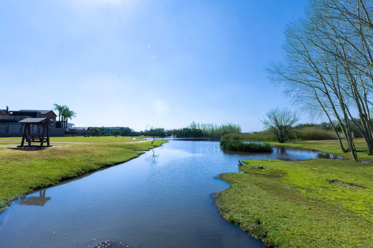A scenic view of a tranquil lake surrounded by well-maintained green lawns and mature trees within a residential estate setting.