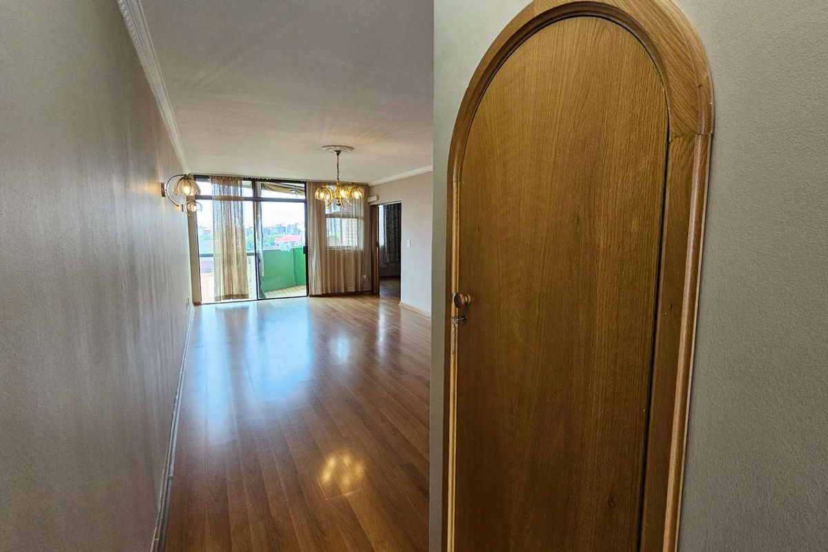 Spacious living area featuring polished timber flooring, arched wooden doorway, and large glass sliding doors leading to an outdoor balcony.