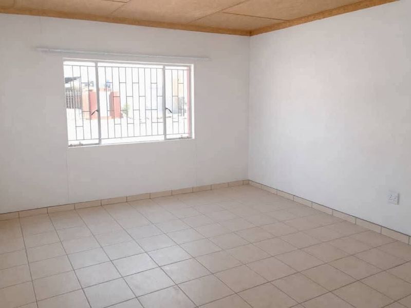 An empty bedroom featuring tiled flooring, white walls, and a window fitted with security bars.