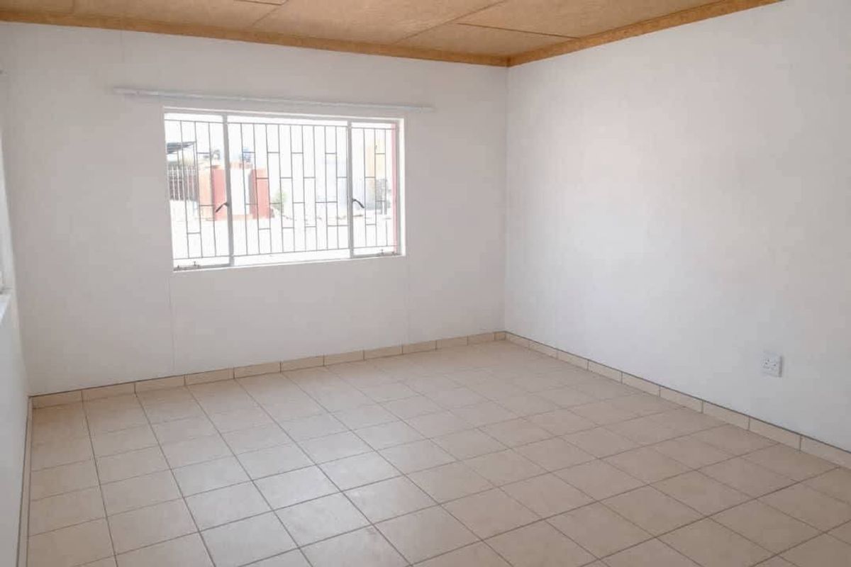 An empty bedroom featuring tiled flooring, white walls, and a window fitted with security bars.