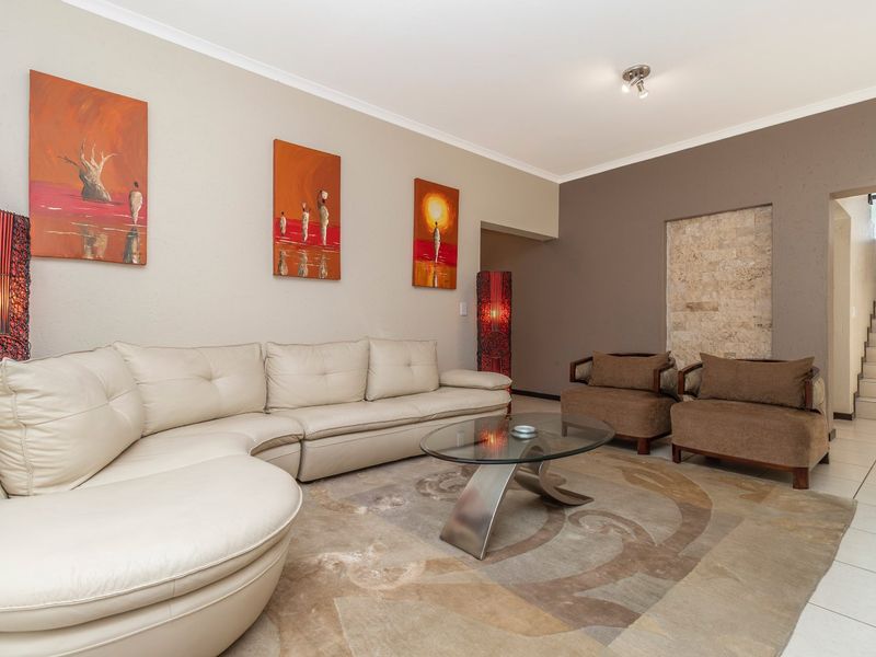 Spacious living room featuring a stone accent wall, neutral tiled flooring, and an open-plan layout leading to an internal staircase.