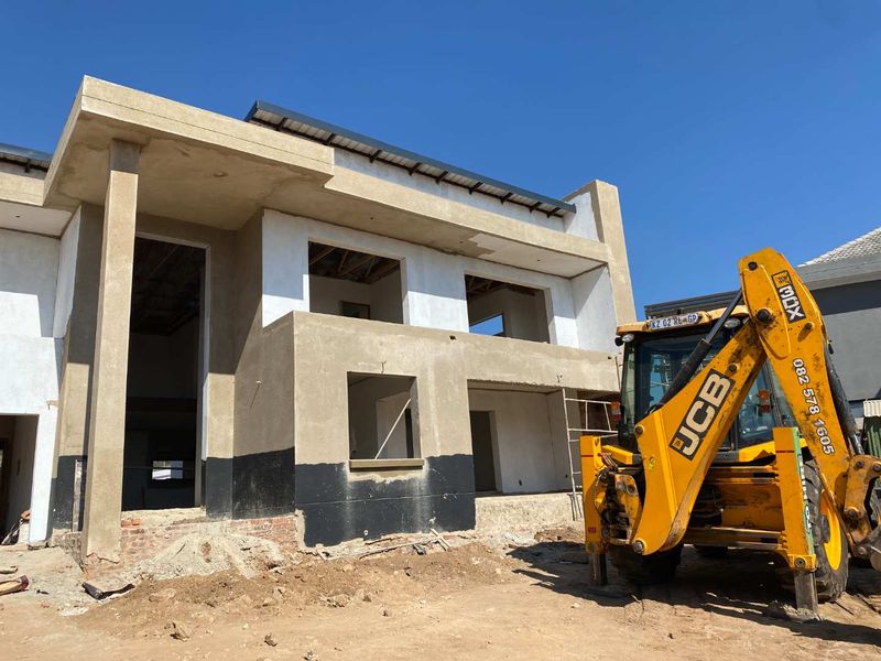 A front view of a double-story residential property currently under construction, featuring plastered walls and exposed structural elements.