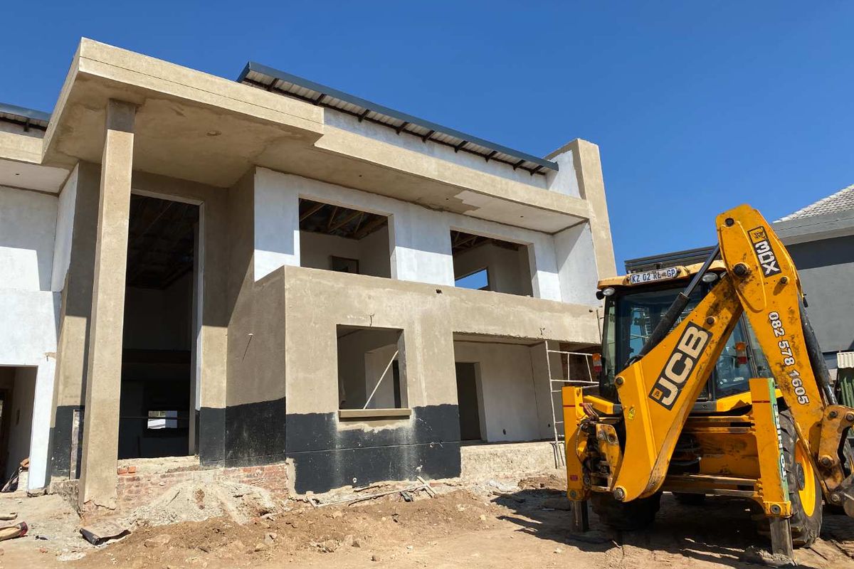 A front view of a double-story residential property currently under construction, featuring plastered walls and exposed structural elements.