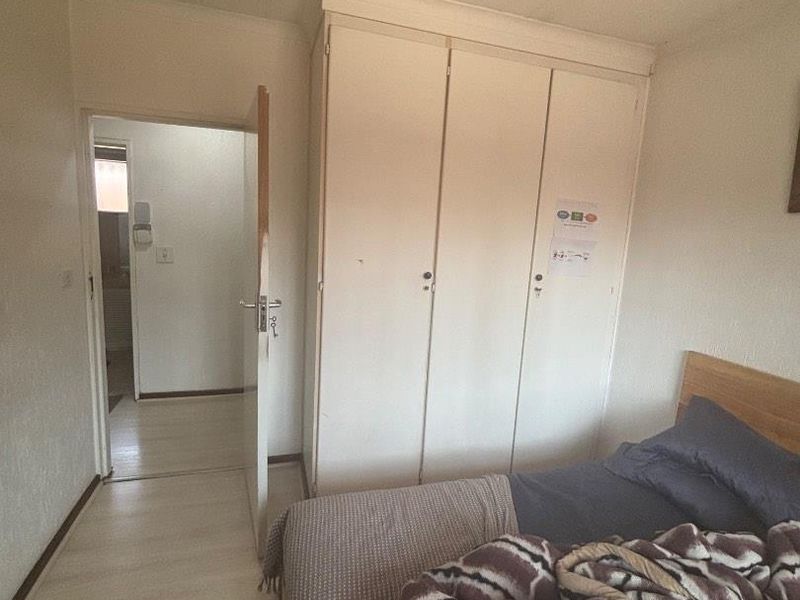 A bedroom featuring built-in cupboards, laminate flooring, and recessed ceiling lighting, providing a functional space with potential for cosmetic updates.