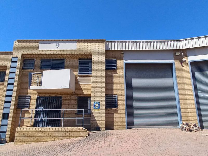 Front elevation of an industrial property featuring brick facade, large roller shutter doors, and secure access points with paved driveway area.