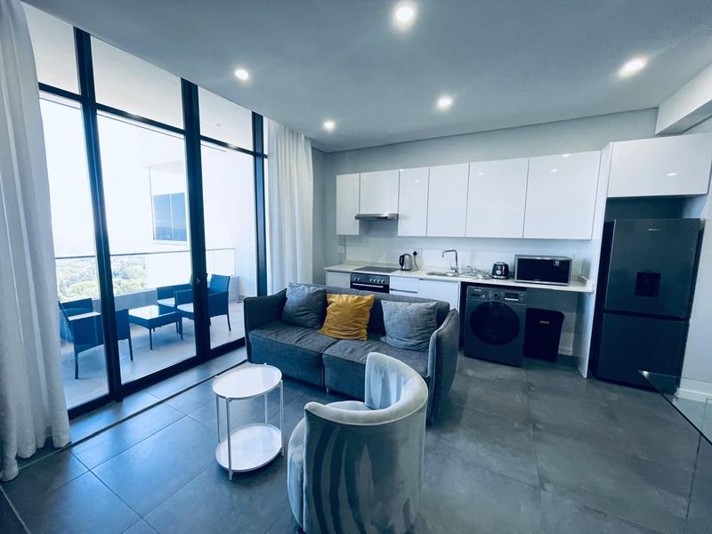 Modern open-plan apartment featuring a sleek kitchen with built-in cabinetry, tiled floors, and floor-to-ceiling glass doors leading to a private balcony.