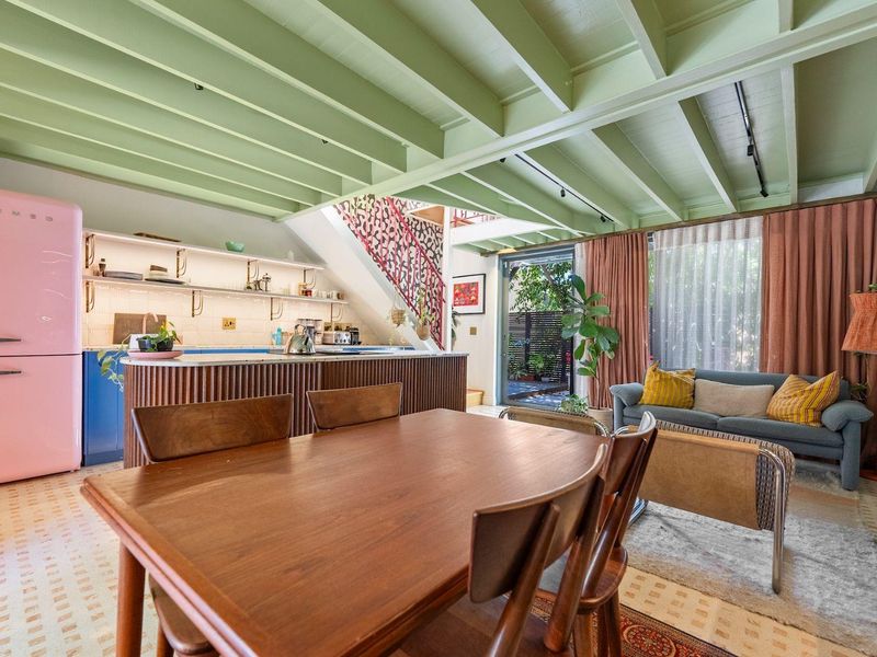 A vibrant open-plan living and kitchen area featuring exposed green timber beams, a modern kitchen island, and direct access to a rear patio.