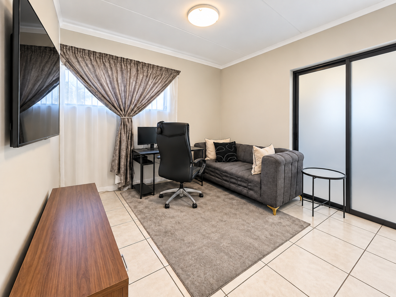 A functional home office space featuring tiled flooring, a modern sliding glass door, and neutral wall finishes.