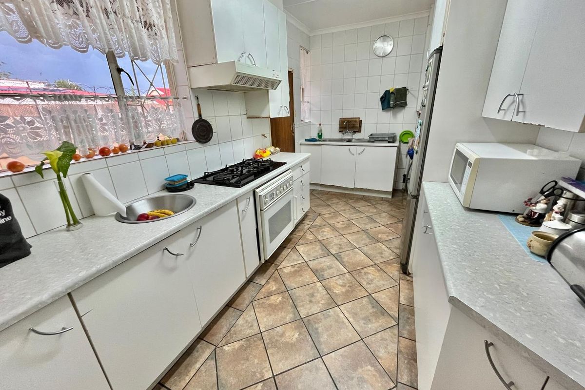 A functional kitchen featuring white cabinetry, tiled splashbacks, a gas hob with extractor fan, and tiled flooring.