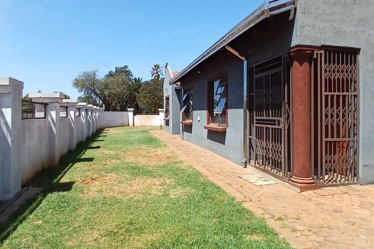 A view of the rear exterior of the house featuring a paved walkway, lawn area, and secure perimeter walling.
