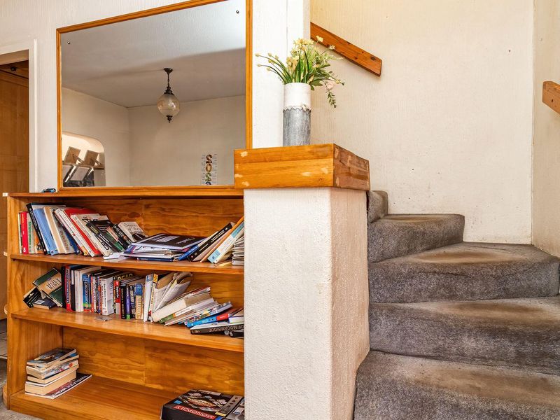 A hallway area featuring a carpeted staircase with a wooden handrail and integrated wooden shelving unit with a wall-mounted mirror.