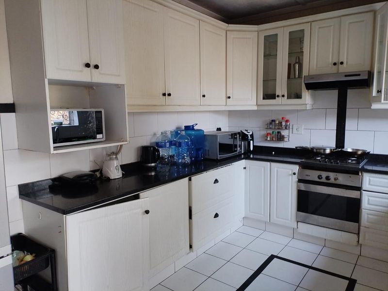 Functional kitchen featuring white cabinetry, granite countertops, tiled backsplash, and integrated appliances including a gas hob, oven, and extractor fan.