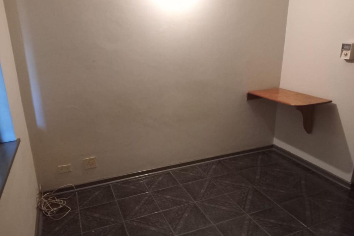 An empty bedroom featuring dark tiled flooring and a built-in wall-mounted wooden desk.