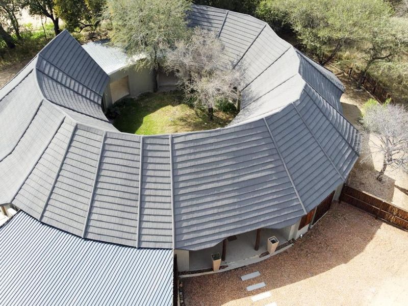 Aerial view of a unique circular house design featuring a central courtyard, tiled roofing, and surrounding natural landscape.