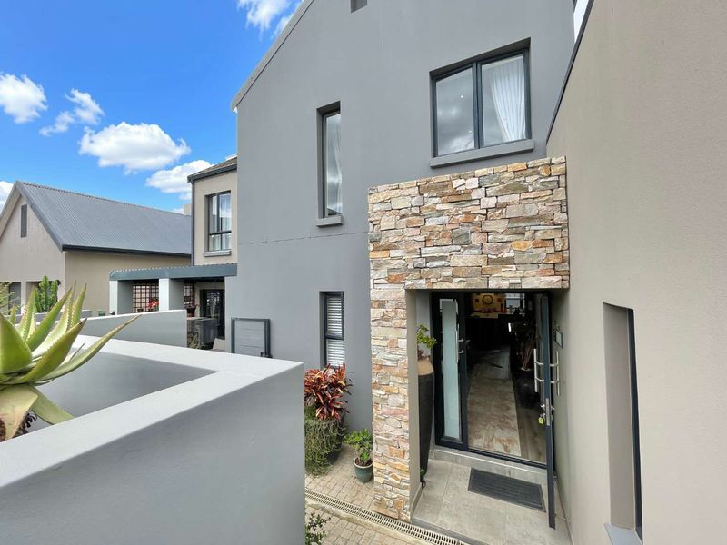 Modern front entrance featuring contemporary grey facade, stone cladding detail, and paved walkway leading to the main door.