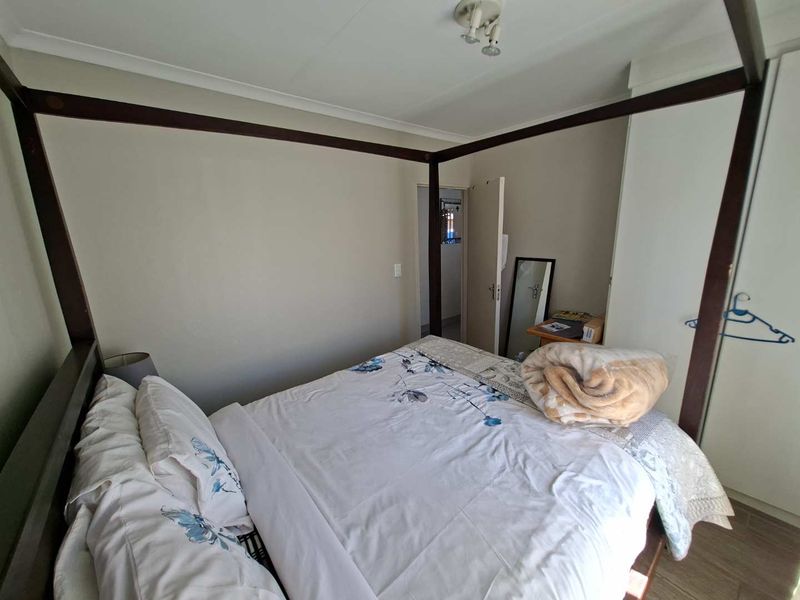 A bedroom featuring built-in wardrobes, laminate flooring, and neutral wall finishes, providing a functional space with direct access to an adjoining room.