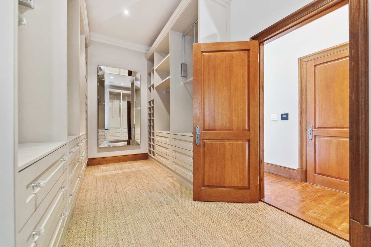 A spacious walk-in dressing room featuring extensive built-in cabinetry, high-quality timber doors, and recessed lighting, presenting a clean and well-maintained finish.