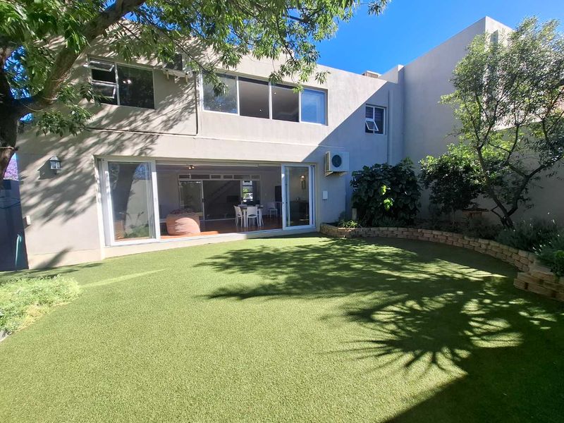 Rear view of the townhouse featuring a landscaped garden with artificial turf, a low retaining wall, and large sliding doors leading to the interior.