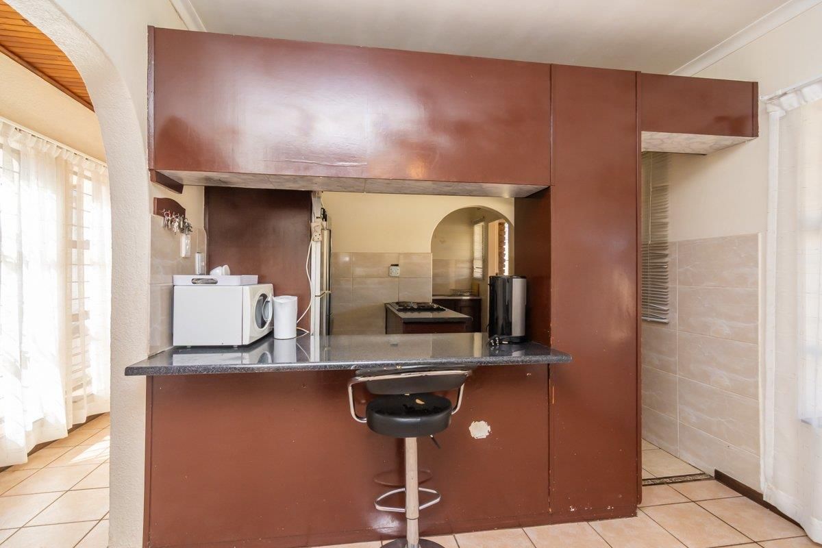 A dated kitchen featuring a breakfast bar pass-through, tiled flooring, and dark brown built-in cabinetry with a view into the adjacent cooking area.