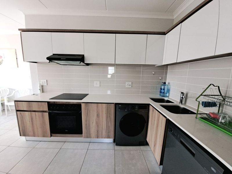 Modern kitchen featuring sleek white and wood-grain cabinetry, stone countertops, integrated appliances, and a tiled backsplash.