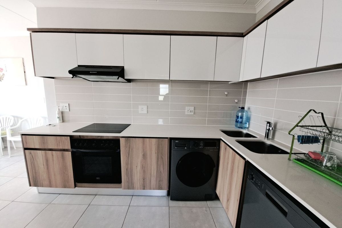 Modern kitchen featuring sleek white and wood-grain cabinetry, stone countertops, integrated appliances, and a tiled backsplash.