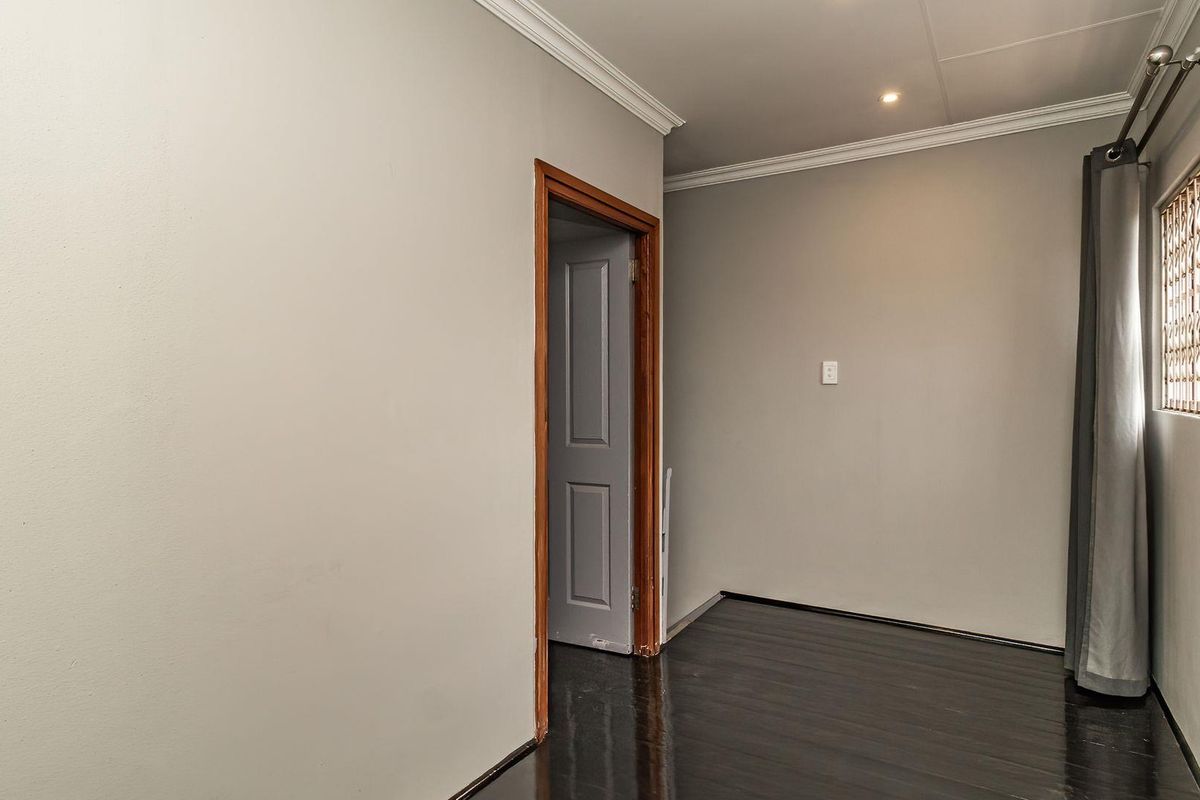 A clean, empty bedroom featuring dark wood laminate flooring, crown molding, and a window fitted with a security gate.