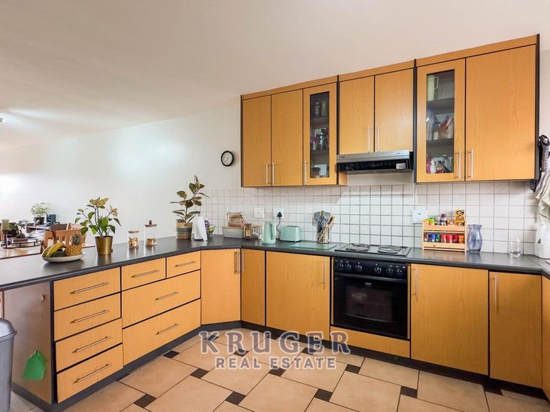 Open-plan kitchen featuring light wood-finish cabinetry, dark countertops, built-in oven and hob, and tiled flooring, flowing into the adjacent dining area.