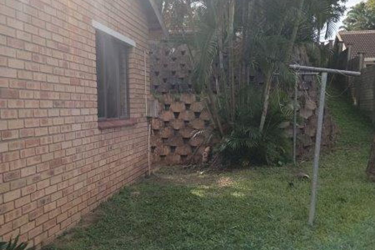 A view of the rear exterior featuring a brick facade, a tiered retaining wall, and a garden area with a rotary clothesline.