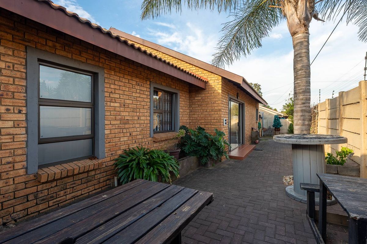 A rear exterior view of the cluster home featuring face-brick walls, paved patio area, and established garden surroundings.