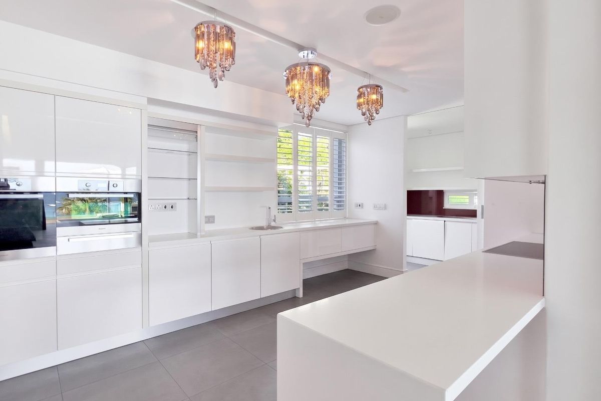 Modern, minimalist kitchen featuring sleek white cabinetry, integrated appliances, quartz countertops, and elegant pendant lighting, offering a clean and functional culinary space.