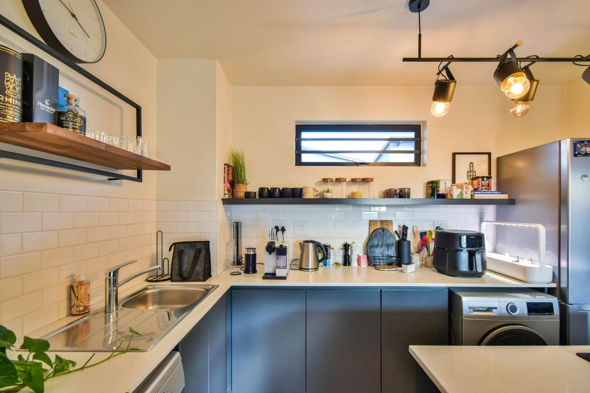 Modern kitchen featuring dark cabinetry, white subway tile backsplash, stone countertops, stainless steel sink, and integrated laundry appliance.