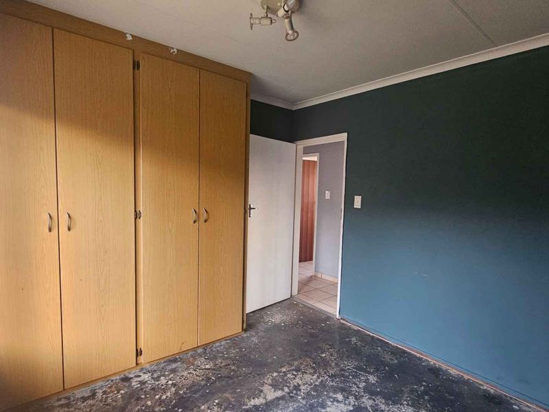 An empty bedroom featuring built-in wooden cupboards and a dark accent wall, requiring flooring repairs or replacement to restore the space.