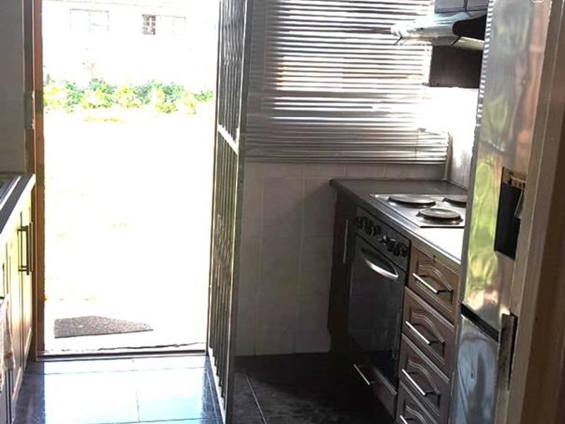 A functional kitchen featuring dark cabinetry, built-in oven and hob, tiled flooring, and direct access to the exterior through a security gate.