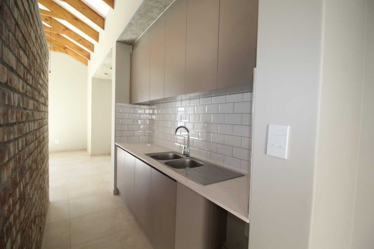 Modern kitchen featuring sleek cabinetry, subway tile backsplash, stone countertops, and a double stainless steel sink, set against a rustic exposed brick wall.