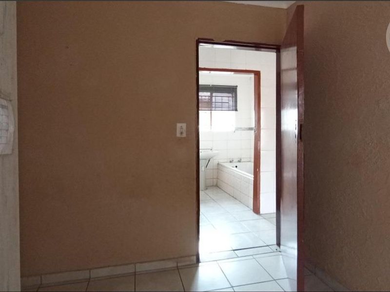 A vacant bedroom featuring tiled flooring and an open doorway leading to an adjacent bathroom with a built-in bathtub.