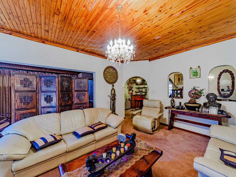 A living room featuring a distinctive timber tongue and groove ceiling, arched architectural openings, and a central crystal chandelier.