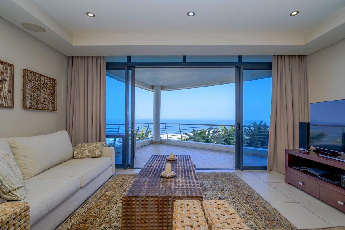 Spacious living room featuring large sliding glass doors that open onto a balcony with expansive ocean views and modern recessed lighting.