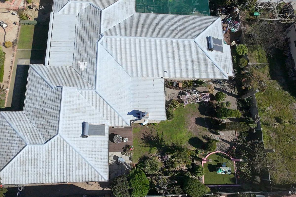Aerial view of the property showing the extensive corrugated metal roof, solar water heating systems, and the surrounding rear garden and patio area.