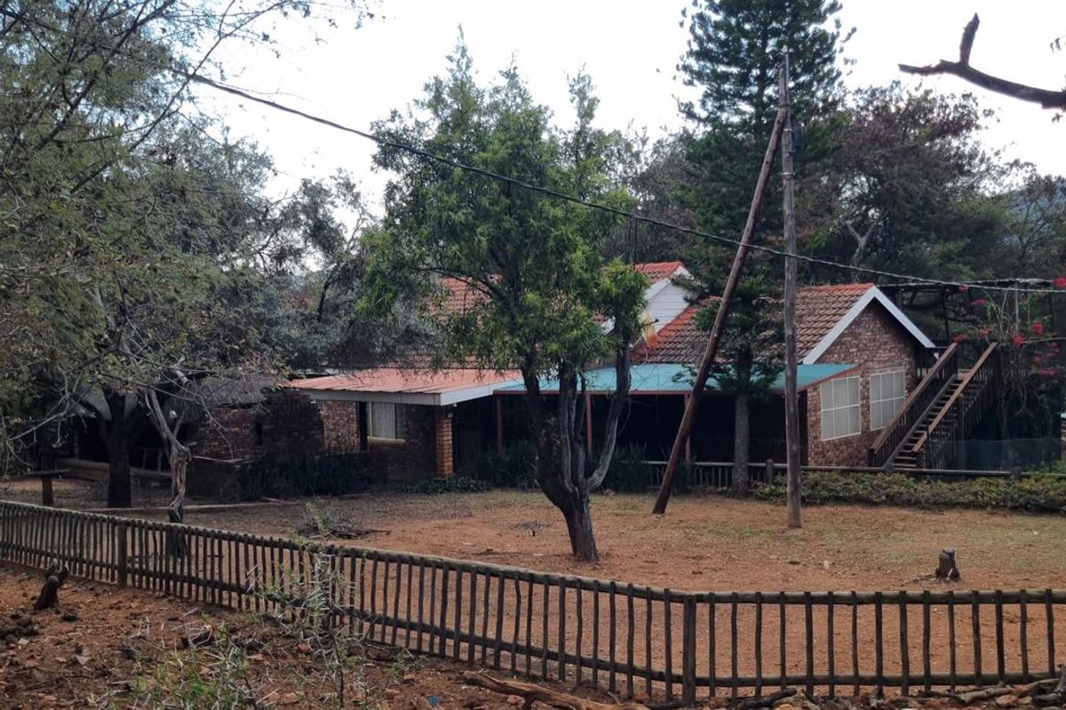 Rear view of a brick house featuring a covered patio, external wooden staircase, and a large, natural garden area with perimeter fencing.