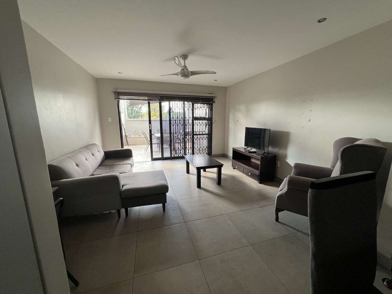 Spacious living room featuring large format floor tiles, a ceiling fan, and sliding glass doors providing access to an outdoor patio area.