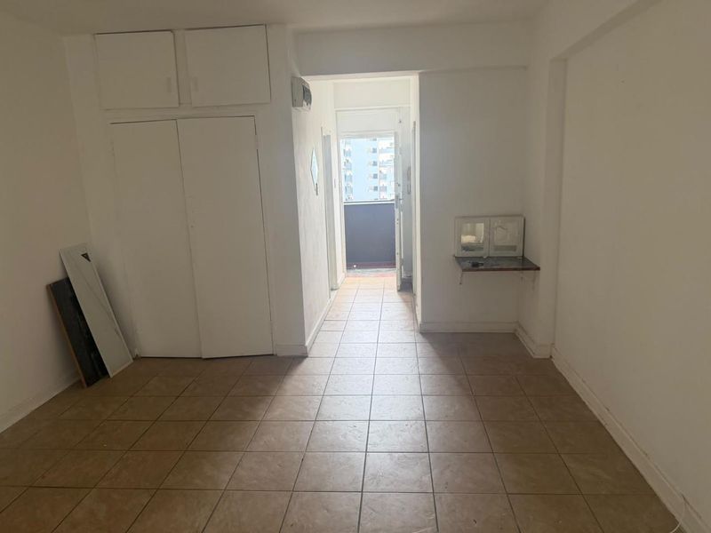 An empty hallway featuring tiled flooring and built-in storage cupboards, leading towards an exterior balcony area.