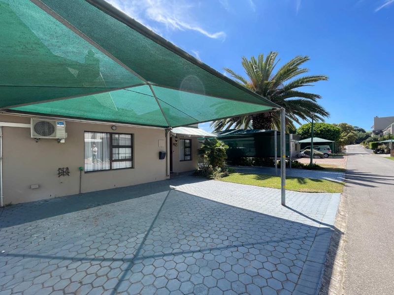 Front exterior view of the property featuring a paved driveway, shade cloth carport, and established garden area.